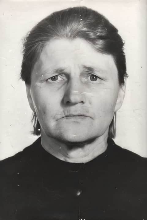 Черно-белая портретная фотография Анны Алексеевны Осиповой, ветерана Великой Отечественной войны. Пожилая женщина с достойной выдержкой смотрит прямо в объектив камеры с серьёзным, задумчивым выражением лица. Её тёмные волосы аккуратно разделены пробором по центру и убраны назад, открывая лицо, изборождённое глубокими морщинами и складками, которые свидетельствуют о десятилетиях стойкости и невзгод. На ней тёмная одежда с высоким воротником, характерная для советской формальной одежды. Винтажная фотография несёт следы времени — тонкие царапины, едва заметные заломы и выцветание, — что придаёт ей подлинный исторический характер и указывает на её происхождение из середины XX века.